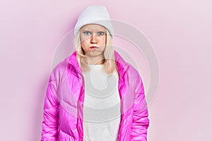 Beautiful caucasian blonde woman wearing wool hat and winter coat puffing cheeks with funny face