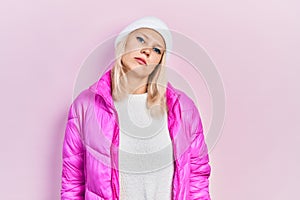 Beautiful caucasian blonde woman wearing wool hat and winter coat relaxed with serious expression on face