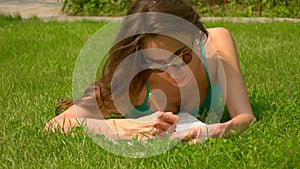 Beautiful caucasian brunette girl laying on the lawn and colorizing picture