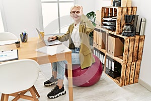 Beautiful caucasian business woman working at the office sitting on pilates ball smiling happy doing ok sign with hand on eye