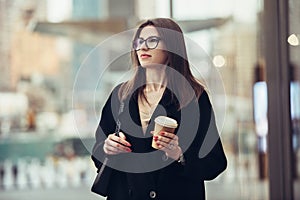 Beautiful caucasian businesswoman walking to the office on city street with coffee cup wearing eyeglasses.