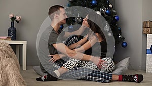 Beautiful caucasian couple in love sitting on the living room floor next to a Christmas tree and decorated boxes