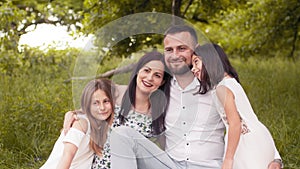 Beautiful caucasian family enjoying summer picnic at green garden. Father, mother and two daughters sitting in hugs on