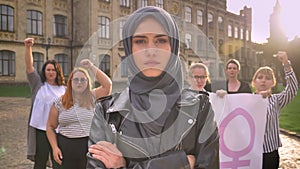 Beautiful caucasian female in hijab standing with crossed hands in the middle of feminists demonstration on the street