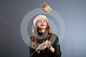 Beautiful caucasian girl in a dress and Santa hat is catching falling presents, looking at camera and smiling, isolated