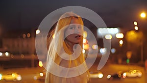 Beautiful Caucasian girl fashion model walking along night city, happy and smiling. Young woman with makeup in a white