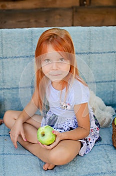 Beautiful caucasian girl of five years old eats green apples in the garden, looks into the camera and smiles. Happy childhood