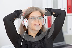 Beautiful Caucasian girl in glasses with her hands behind her head listening to music on headphones.