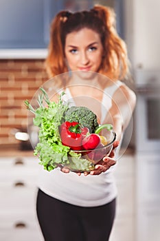 Beautiful caucasian girl holding glasses bowl with ingredients for low-caloric vegetables salad on kitchen.