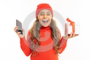Beautiful caucasian girl holds a white box with gift in one hand and a smartphone in other hand, smiles and choises