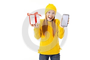 Beautiful caucasian girl holds a white box with gift in one hand and a smartphone in other hand, smiles and choises