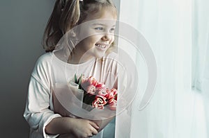 Beautiful caucasian girl looking at window empty space. Kid with flowers bouquet.Mother's day. Women's day.Birthday