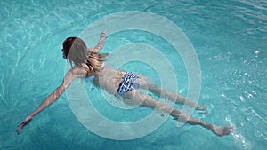 Beautiful Caucasian model, young woman is swimming in a pool with blue water in a hotel, under the open sky. The concept