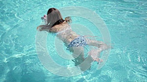 Beautiful Caucasian model, young woman is swimming in a pool with blue water in a hotel, under the open sky. The concept