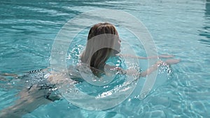 Beautiful Caucasian model, young woman is swimming in a pool with blue water in a hotel, under the open sky. The concept