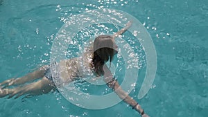 Beautiful Caucasian model, young woman is swimming in a pool with blue water in a hotel, under the open sky. The concept