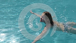Beautiful Caucasian model, young woman is swimming in a pool with blue water in a hotel, under the open sky. The concept