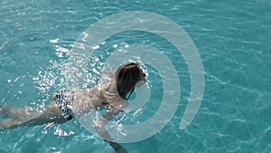 Beautiful Caucasian model, young woman is swimming in a pool with blue water in a hotel, under the open sky. The concept