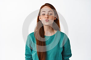 Beautiful caucasian redhead girl kissing, pucker lips and leans for kiss, romantic relationship or date, standing flirty