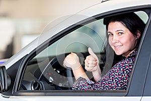 Beautiful caucasian smiling brunette woman sitting in the new car and showing thumbs up. Consumerism concept