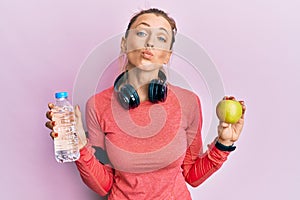 Beautiful caucasian sports woman holding water bottle and green apple looking at the camera blowing a kiss being lovely and sexy