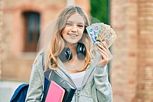 Beautiful caucasian student teenager using headphones holding canadian dollars at the city