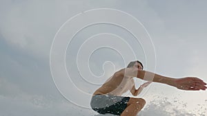 A beautiful Caucasian surfer actively rakes the wave starts and rides it. A young guy is surfing in the ocean and doing