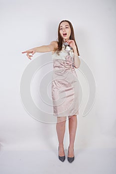 Beautiful caucasian teen girl stands in a short evening dress and mocks the interlocutor, humiliating, on a white background in th