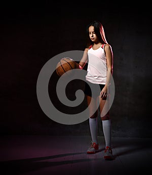 Beautiful caucasian teen woman in sportswear playing basketball . Sport concept isolated on black background