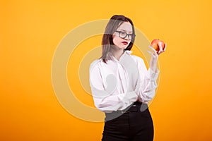 Beautiful caucasian teenage girl holding and looking at a red apple in studio over yellow background