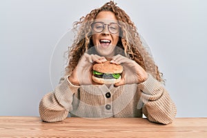 Beautiful caucasian teenager girl eating a tasty classic burger smiling and laughing hard out loud because funny crazy joke