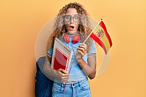 Beautiful caucasian teenager girl exchange student holding spanish flag afraid and shocked with surprise and amazed expression,