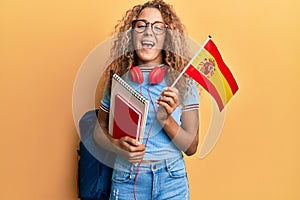 Beautiful caucasian teenager girl exchange student holding spanish flag smiling and laughing hard out loud because funny crazy