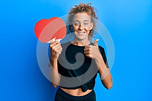 Beautiful caucasian teenager girl holding red ping pong rackets smiling happy and positive, thumb up doing excellent and approval
