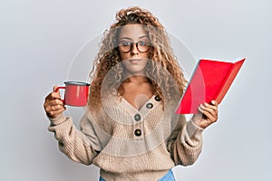 Beautiful caucasian teenager girl reading a book and drinking a cup of coffee relaxed with serious expression on face