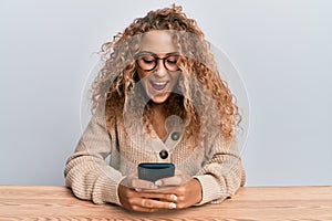 Beautiful caucasian teenager girl using smartphone sitting on the table smiling and laughing hard out loud because funny crazy