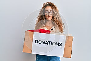 Beautiful caucasian teenager girl volunteer holding donations box relaxed with serious expression on face