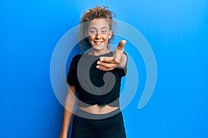 Beautiful caucasian teenager girl wearing black sportswear smiling friendly offering handshake as greeting and welcoming