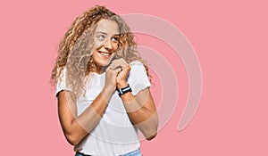 Beautiful caucasian teenager girl wearing casual white tshirt laughing nervous and excited with hands on chin looking to the side