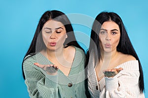 Beautiful caucasian twin girls blow a kiss to the camera. Blue background