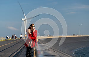 Beautiful Caucasian waman with sunglasses stand in front of wind turbine or windmill also look to right side near the road with