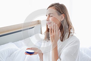 Beautiful caucasian woman applying moisturizer cream on face