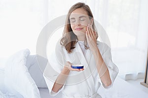 Beautiful caucasian woman applying moisturizer cream on face