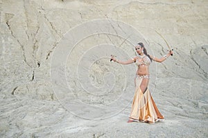 Beautiful Caucasian woman belly dancer posing in desert with swords