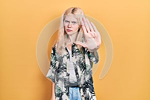 Beautiful caucasian woman with blond hair wearing tropical shirt doing stop sing with palm of the hand