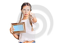 Beautiful caucasian woman with blonde hair holding empty frame pointing with finger to the camera and to you, confident gesture