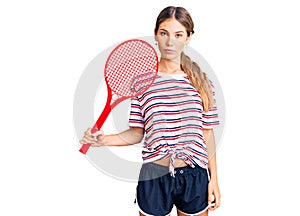 Beautiful caucasian woman with blonde hair playing tennis holding racket thinking attitude and sober expression looking self