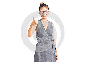 Beautiful caucasian woman with blonde hair wearing business clothes and glasses doing happy thumbs up gesture with hand