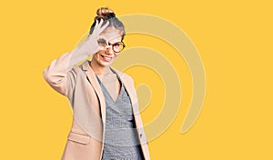 Beautiful caucasian woman with blonde hair wearing business jacket and glasses smiling happy doing ok sign with hand on eye