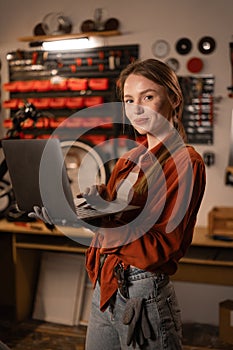 Beautiful caucasian woman in casual clothes using laptop and smiling in bicycle repair shop